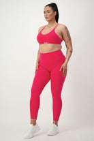 A woman stands against a plain background wearing a bright pink sports bra and DRIVEN Gym Apparel's Classic Full Length Tights (cherry). She has a full ponytail and several tattoos on her arms. Sporting white sneakers, her gym wear exudes confidence.