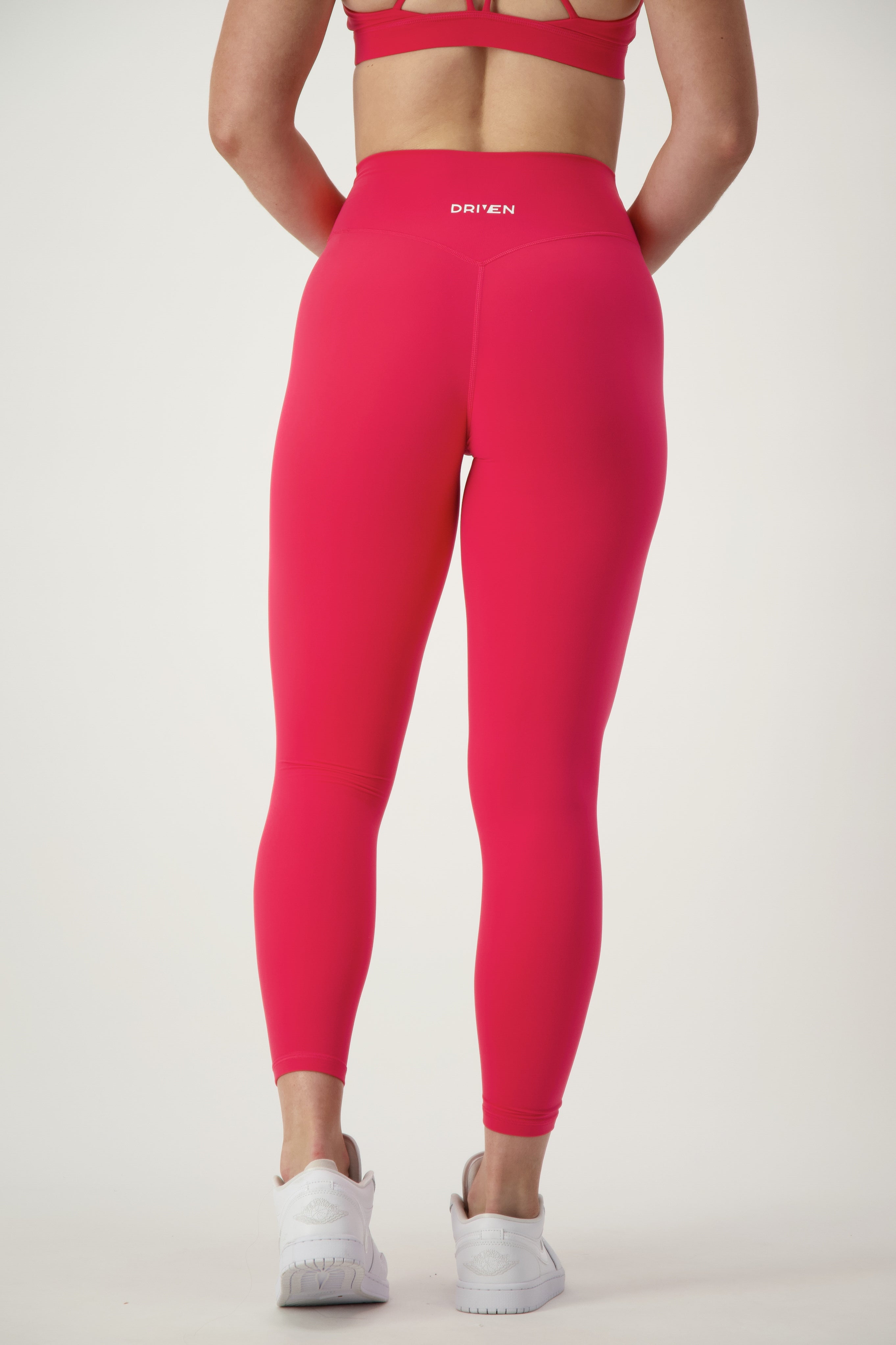 A person is standing with their back to the camera wearing coordinating red activewear: a sports bra and high-waisted Classic Full Length Tights (cherry) featuring "DRIVEN" on the waistband. They're also sporting white athletic shoes, set against a plain white background, from DRIVEN Gym Apparel.