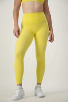 A person wearing bright yellow DRIVEN Gym Apparel Classic Full Length Tights (lemon) and a matching yellow sports bra is standing against a plain background, embodying the essence of athleisure. They are also wearing white sneakers. Only the person's torso and legs are visible.