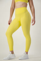 A person wearing a yellow sports bra and DRIVEN Gym Apparel's Classic Full Length Tights (lemon) stands in a neutral pose. They are also wearing white athletic shoes. The background is plain and light-colored. The image focuses on the fitness apparel from the shoulders down, highlighting trendy athleisure wear.
