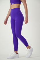 A person showcases chic athleisure in a matching purple sports bra and Classic Full Length Tights (sapphire), paired with white sneakers. Their torso and legs stand out against a plain white background, with the branding "DRIVEN Gym Apparel" on the sports bra.