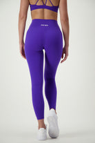 A person in a purple athletic outfit, seen from the back, is standing on a neutral background. They are wearing a sports bra and Classic Full Length Tights (sapphire) with the brand name "DRIVEN Gym Apparel" visible on the waistband. This stylish activewear ensemble is completed with white sneakers.