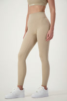 A person wearing DRIVEN Gym Apparel's taupe Classic Full Length Tights and a matching sports bra, epitomizing athleisure. They are also sporting white athletic shoes against a plain, light-colored background. The person's head is not visible in the image.