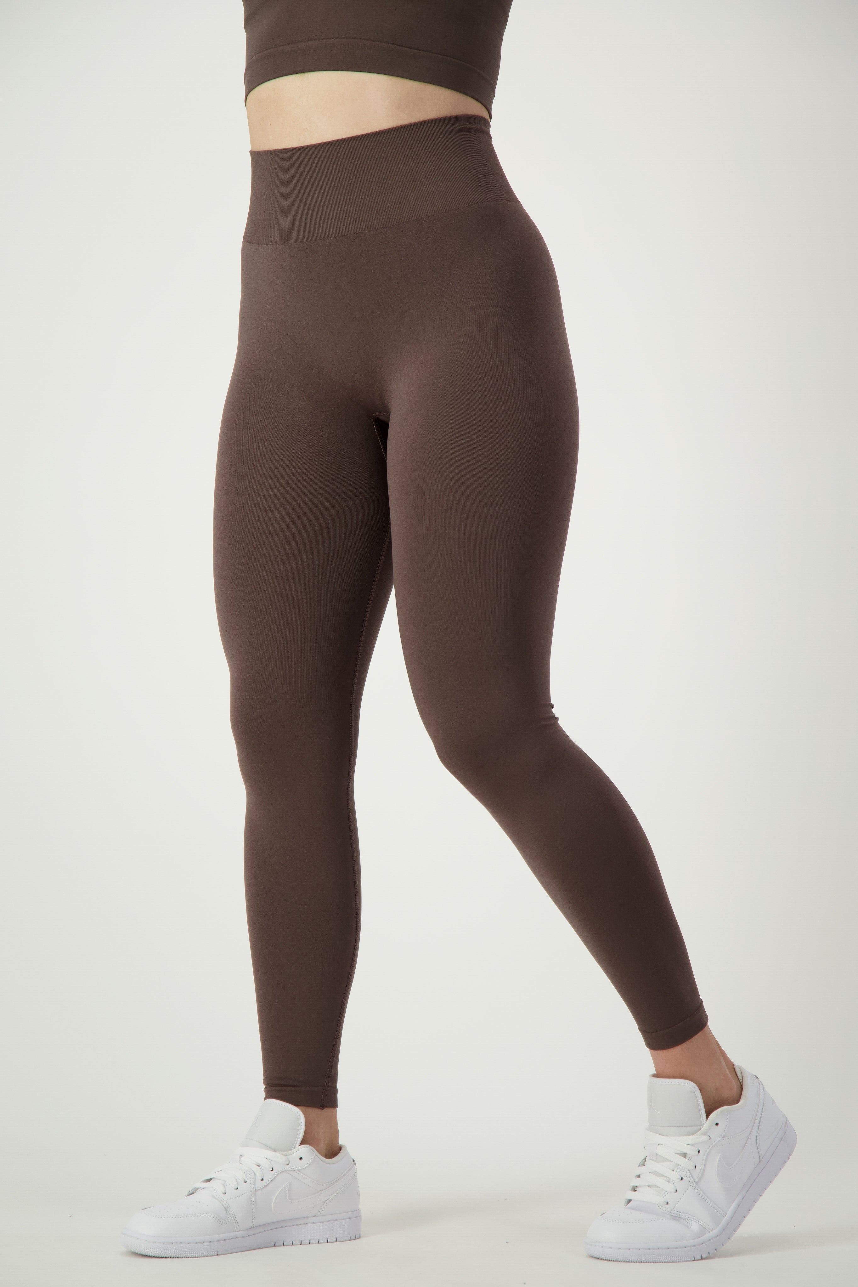 A person is wearing SL Flex Full Length Tights (mocha) by DRIVEN Gym Apparel, a matching brown sports bra, and white sneakers. The image is focused on the lower half of the body from the waist down, highlighting the fitness apparel against a plain white background.