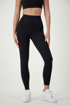 A person wearing black Phone Pocket Tights from DRIVEN Gym Apparel and a matching black cropped top stands against a plain light background. They are also wearing white sneakers, showcasing their gym wear from shoulders to ankles with a focus on the sleek athleisure style.