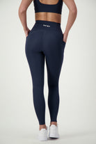 A person wearing navy Phone Pocket Tights with the brand name "DRIVEN Gym Apparel" visible on the waistband stands with their back to the camera, hands in pockets. They are also sporting white sneakers, perfectly blending style and comfort in chic fitness apparel.